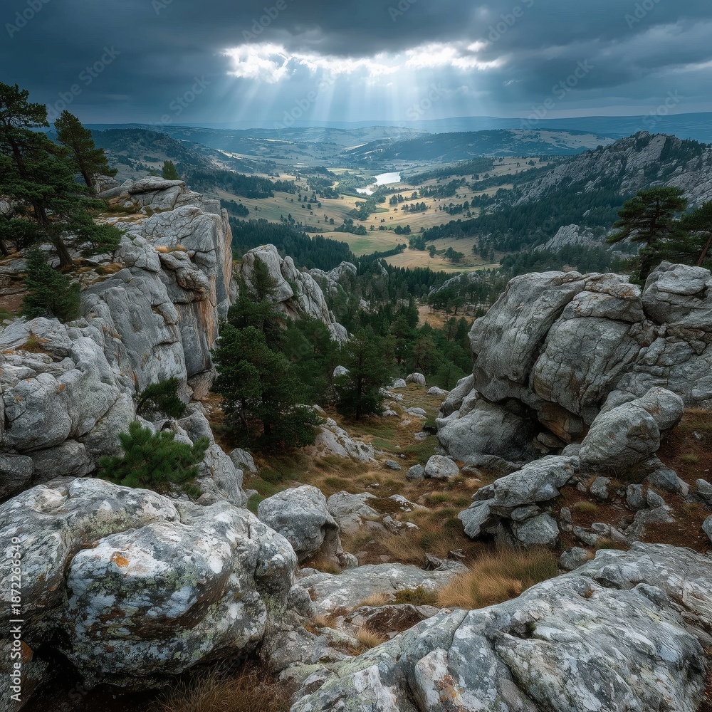 Obraz premium Sunbeams break through clouds, illuminating a lush valley of forests and rocky cliffs with serene grandeur.