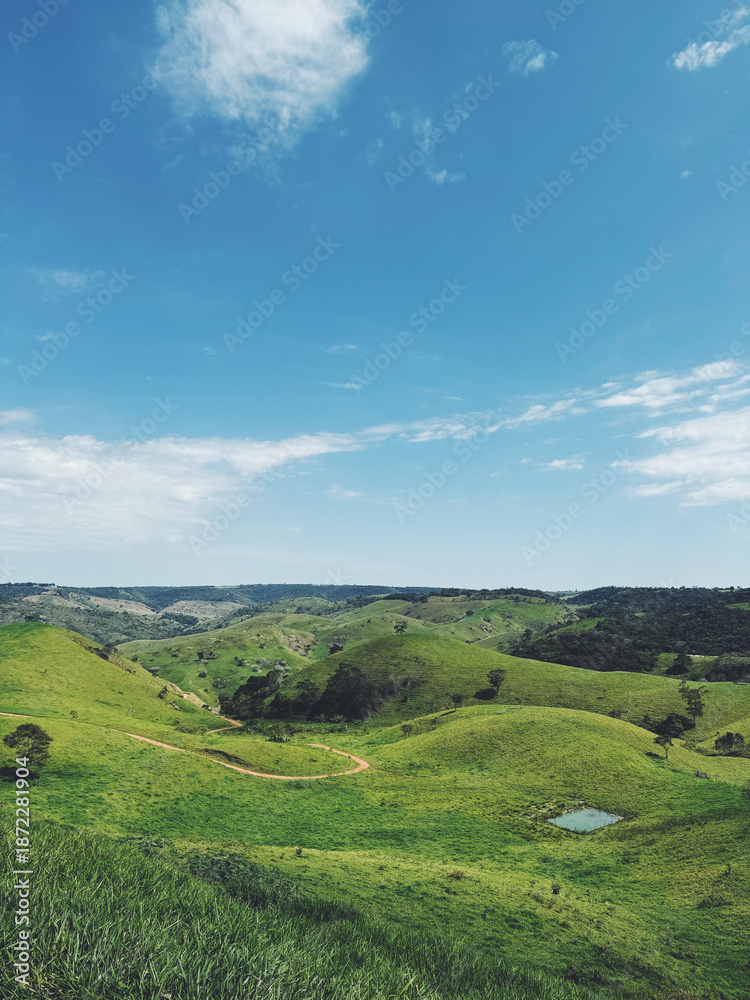 Fototapeta premium Green rolling hills landscape with rural path under blue sky