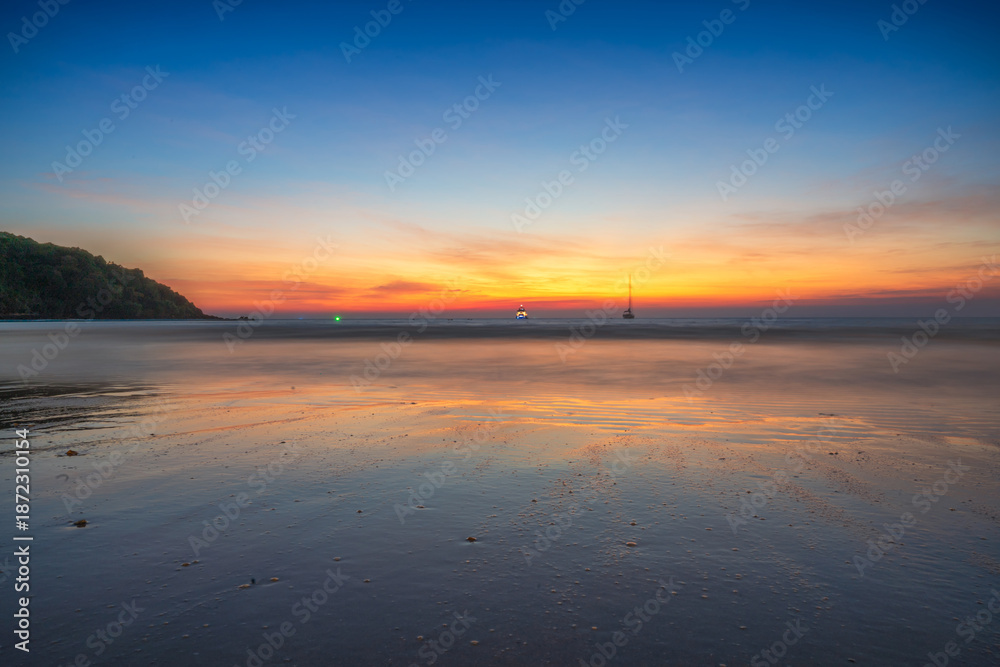 Obraz premium Beautiful tropical beach at sunset with golden light reflecting on the wet sand under a vibrant twilight sky