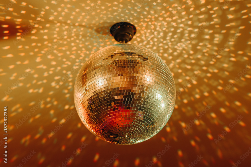 Obraz premium disco ball with mirror surface and bright rays, orange color, hanging on ceiling, night party background