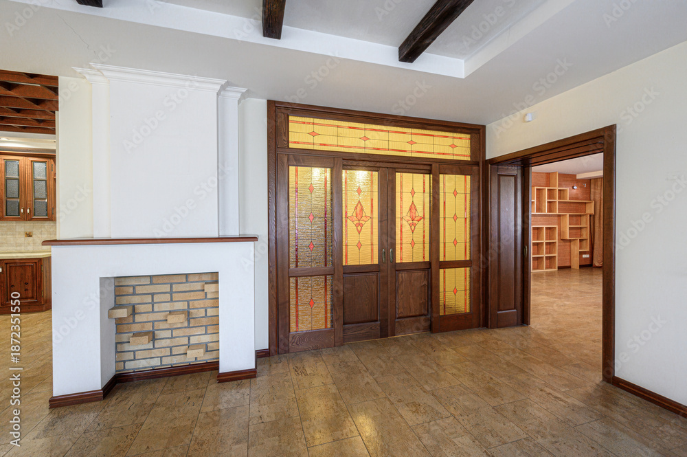 Obraz premium Spacious room with a white fireplace featuring brick interior, stained-glass wooden doors, tiled flooring, exposed wooden ceiling beams, open doorways to a shelved area