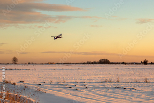 A plane takes off over a snow-covered field during sunset