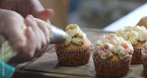 A pastry chef at work. Close-up on hands using a piping bag to frost a cupcake on a wooden board. Confectionery and cooking hobby concept.