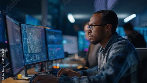 Medium shot of a cyber threat expert using multiple screens to gather and assess data on sophisticated attacks against public utility control systems.