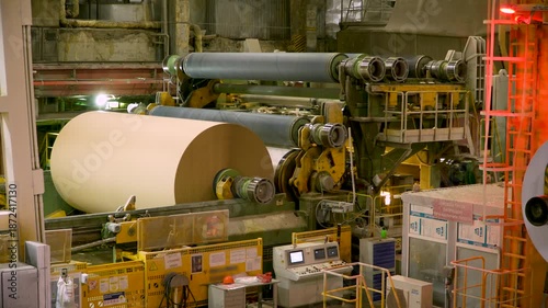 A cardboard production machine. In the foreground, a crane moves a roll of white paper