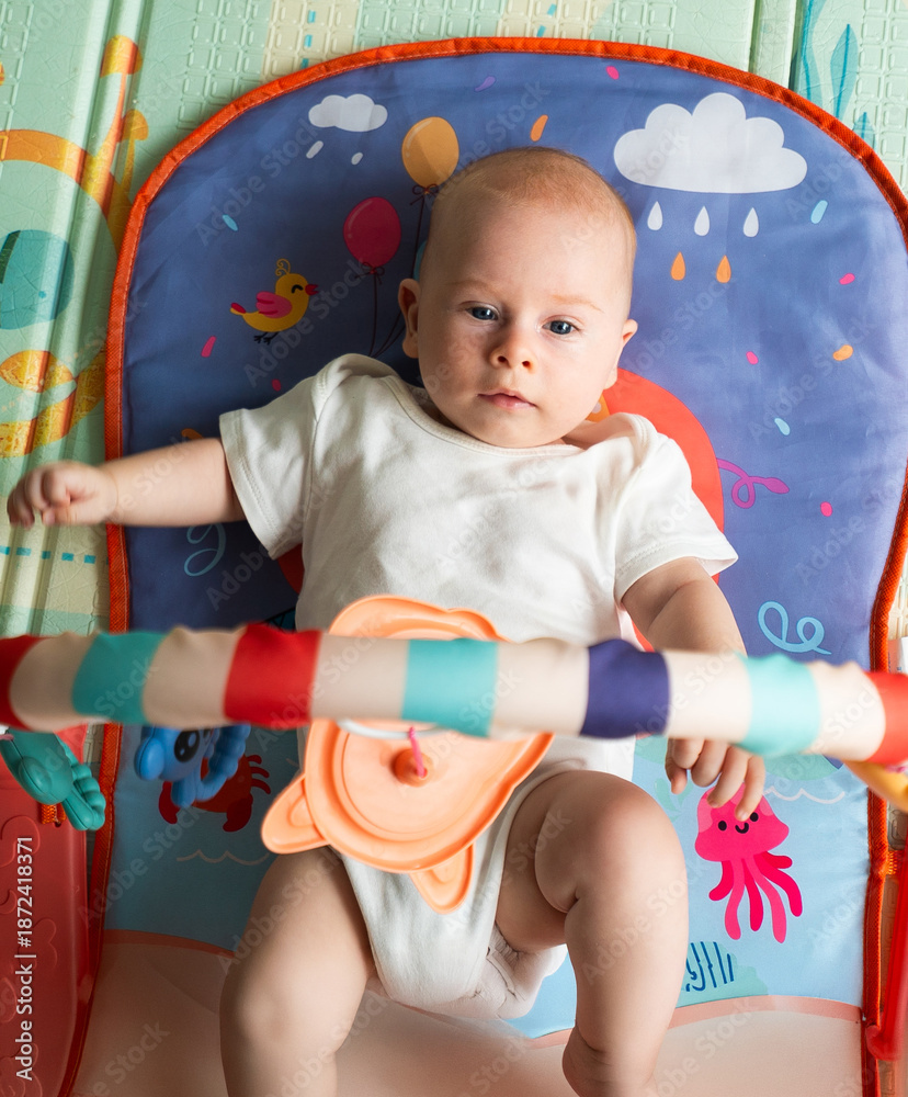 Fototapeta premium A baby is laying on a mat with a toy in his hand