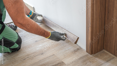 Installing elegant plastic baseboard, showcasing skilled craftsmanship in home improvement and renovation. Detailed view of pro floating floor work, fitting trim for seamless interior finish.