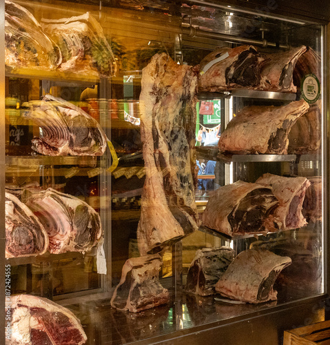 Great display of large joints of beef hanging in fridge. Dry ageing cabinet with beef meat in cold storage. Dry-aged cuts of raw meat. Food manufacturing.