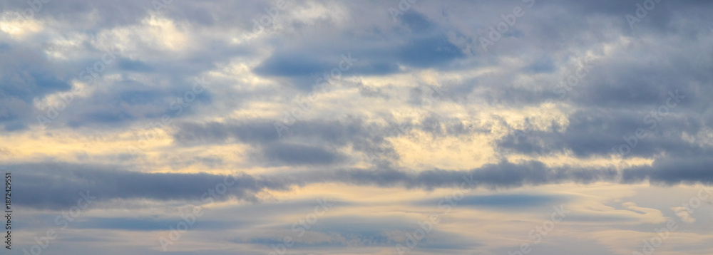 Fototapeta premium Scenic panoramic sky with layered gray clouds and golden sunlight peeking through the clouds during sunrise or sunset