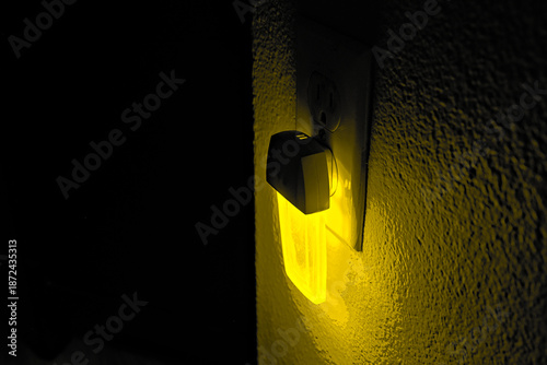 Tableau sur toile Yellow night light glowing from a wall outlet in a dark interior, conveying warm ambient illumination, nighttime safety, and home comfort