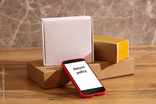 Fotografie stack of boxes on table and smartphone with Return policy on screen