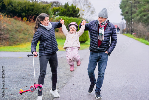 Billede på lærred Uplifted moment senior man and mother lifting laughing child by the hands while