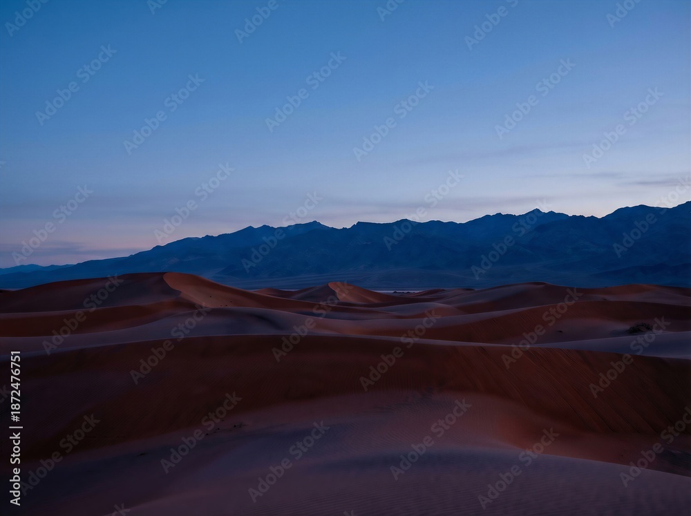 Fototapeta premium Red desert dunes meeting a dark blue mountain range at twilight