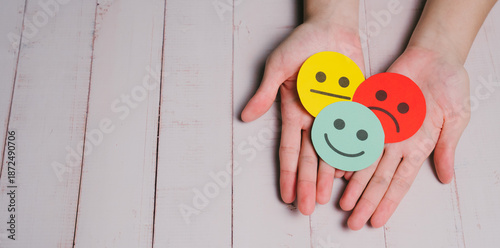 Feedback concept. Happy face Sad face Neutral face Emotion Paper cutouts Hand holding Wooden background Positive emotion Negative emotion Mixed feelings