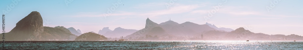 Obraz premium Panoramic Rio de Janeiro seascape with Sugarloaf Mountain and Corcovado silhouette, sparkling Guanabara Bay, pastel morning sky, haze and distant skyline, Brazil