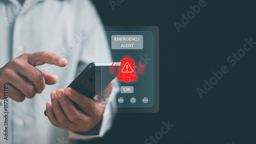 Emergency alert concept. Hand using smartphone with warning notification and alert icon on screen. Crisis notification, emergency response, risk management, mobile technology, public safety system.