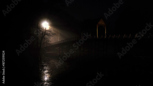 Covered bridge at night with reflective water and streetlamp