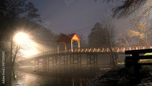 Wooden bridge and gazebo illuminated in thick night fog