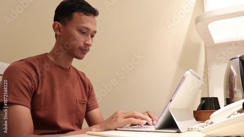 An Asian man typing on a tablet at a table