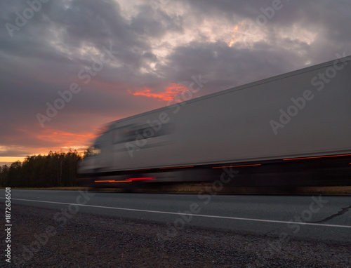 Large truck moving quickly along a highway during a vibrant sunset with dramatic clouds in the background