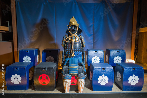 фотографія Elaborate Japanese samurai armor set showcased indoors at Himeji Castle, surrounded by decorative blue and black boxes with floral emblems under soft lighting