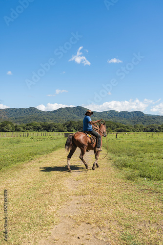 Fotografie Costa Rican cowboy riding horse in vast green field under blue sky