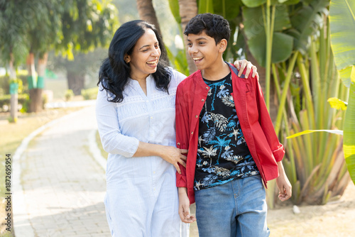 Young Indian mother and son laughing and walking together at outdoor summer park. sharing and talking to each other, family bonding and carefree togetherness. Parenthood
