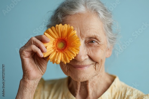 Wallpaper Mural Elderly woman with gray hair playfully covers one eye with a vibrant orange blossom Torontodigital.ca