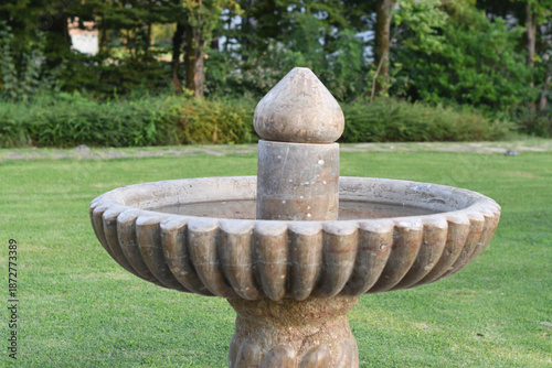Tableau sur toile Weathered stone birdbath in lush green garden setting outdoors
