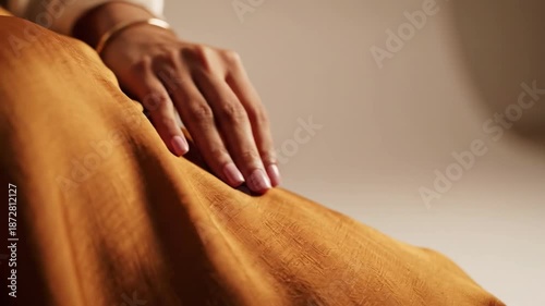 Woman's hand resting on orange fabric with gold bracelet