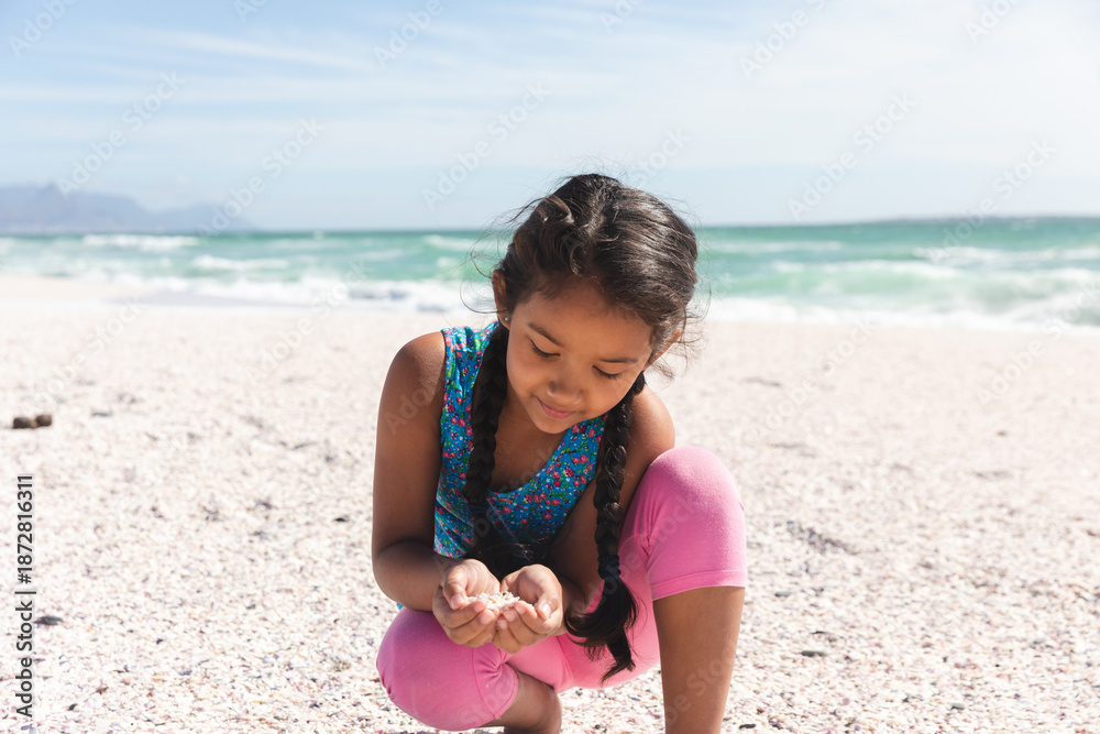 Fototapeta premium Cute little girl holding sand in cupped hands while playing at beach on sunny day