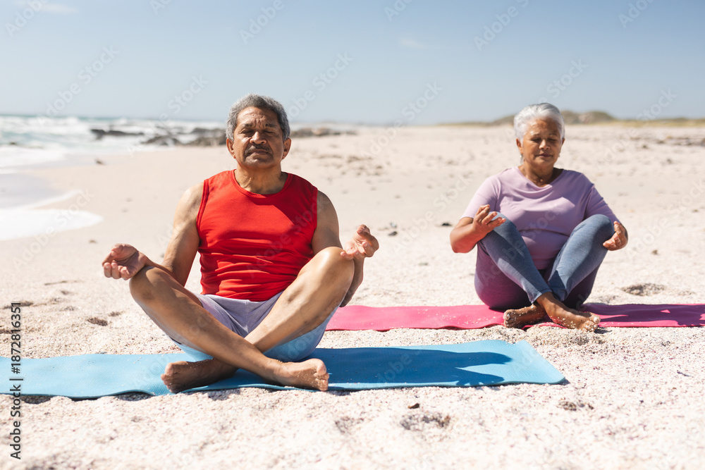 Fototapeta premium senior couple meditating on yoga mats at beach against sky during sunny day