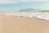 Sea wave foam on shore at sunny beach with mountains in distant background