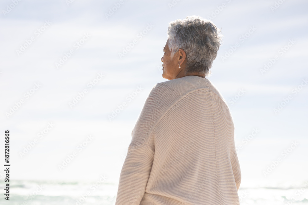 Naklejka premium Rear view of retired senior woman looking at sea against sky from beach on sunny day