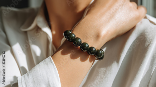 Close up of person wearing dark green beaded bracelet on their wrist, dressed in white shirt, with soft natural light highlighting smooth skin and shiny beads