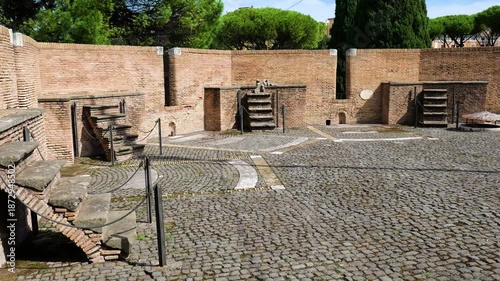 quiet interior courtyard curved cobblestone paving low brick walls niches stone stairways lead elevated platforms framed by tall trees castel sant'angelo to rome italy hadrian's mausoleum 