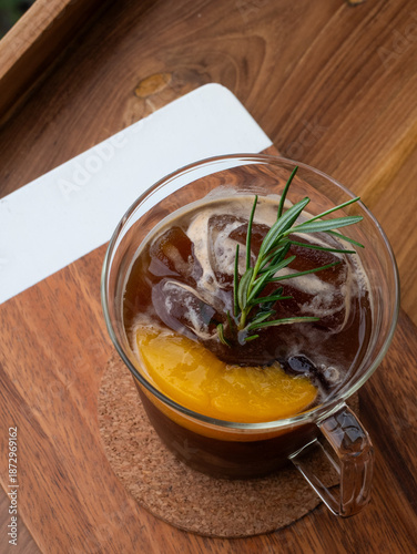 Glass Mug of Citrus Coffee with Ice and Rosemary Garnish on Wooden Table