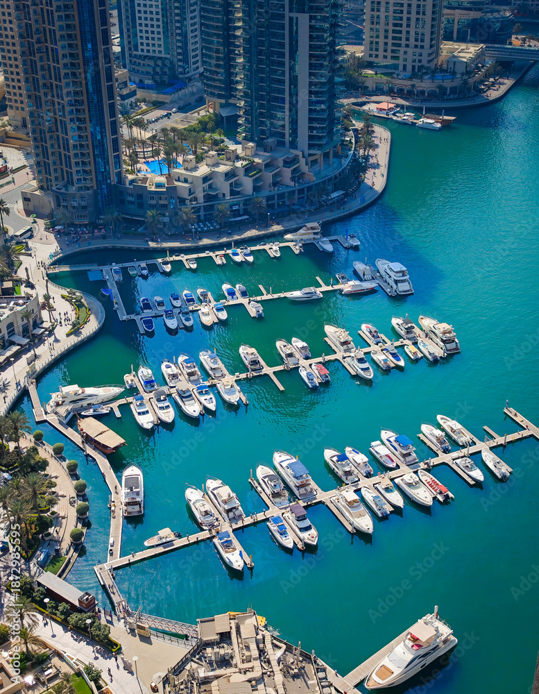 Fototapeta premium Aerial drone view of Dubai Marina harbor with many luxury yachts, capturing modern waterfront and city skyline. Floating boats on canal