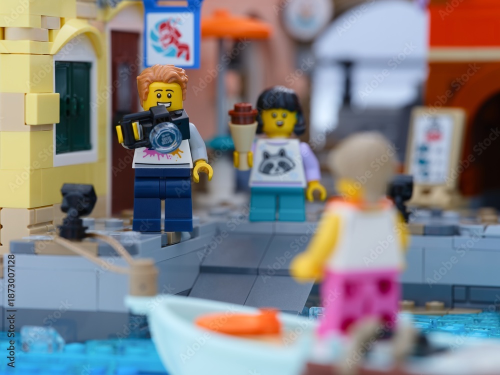 Fototapeta premium Tambov, Russian Federation - January 05, 2026 Lego man minifigure with camera and a girl with ice cream standing on a dock and looking to a woman in boat.