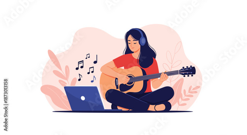 Young woman wearing headphones takes an online music lesson, sitting cross-legged on the floor while playing an acoustic guitar in front of her laptop.