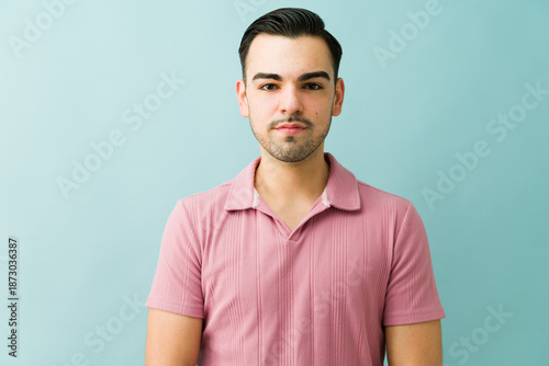 Confident hispanic man posing for portrait, standing against blue background with serious expression