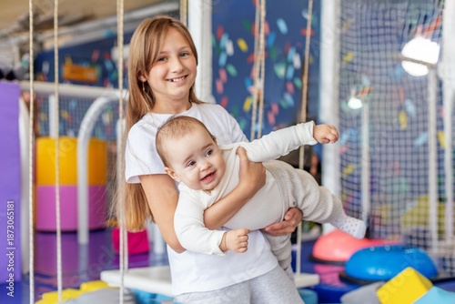Foto Smiling girl holding baby brother in playroom. Family time