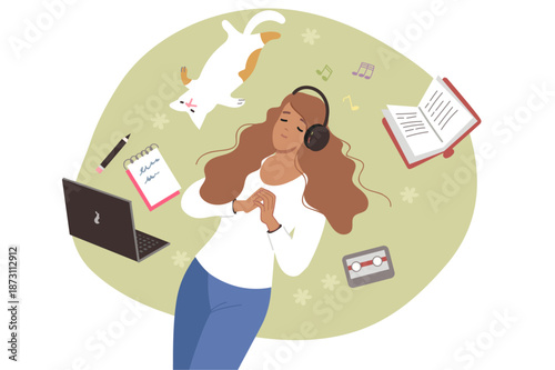 Woman listens to music on headphones, lies on lawn near cat and textbooks and takes break from work. Young girl student or freelancer enjoying relaxing music or educational audio book