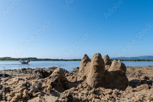 Sandcastle on.a beach with a dog playing in the water in the background