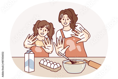 Mom and daughter are preparing breakfast or pastries and with smile show palms stained with flour. Woman brings up little girl teaching how to cook pastries from dough and enjoys raising child