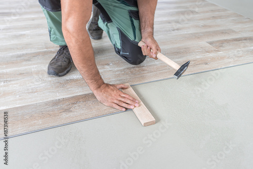 Floating floor work. The worker taps the board of vinyl plank to lock the click system. He is using hammer and wooden plank.