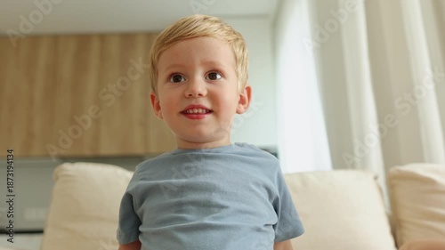 Close-up of a happy toddler boy with blond hair smiling and looking at the camera indoors