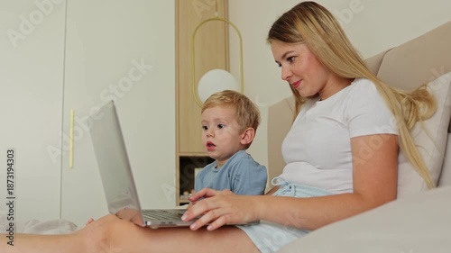 A young mother and her adorable child share a sweet moment watching educational content on a laptop while relaxing in bed