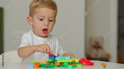 Adorable toddler boy actively engaged in building a structure using vibrant plastic blocks on a white table. childhood development, focus, and imaginative play in a bright home setting.