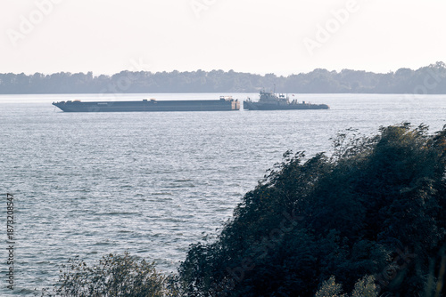 Cargo barge pushed by tugboat on wide river with distant forest shoreline